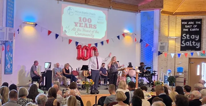 Worship leaders speaking from the platform during Milton Baptist Church's centenary service.