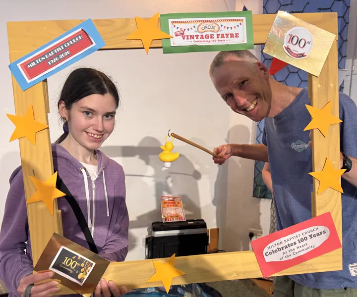 Two visitors smiling with a hook-a-duck prize in the Vintage Fayre photograph frame.