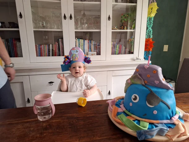 Elianne wearing a party hat beside her first birthday cake.