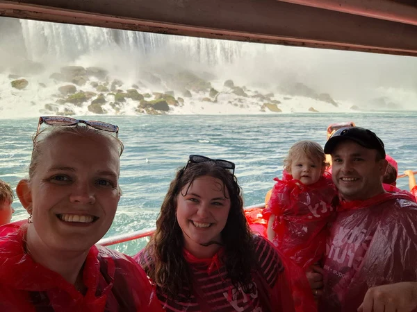 The family and a friend wearing rain ponchos on a boat near a waterfall.
