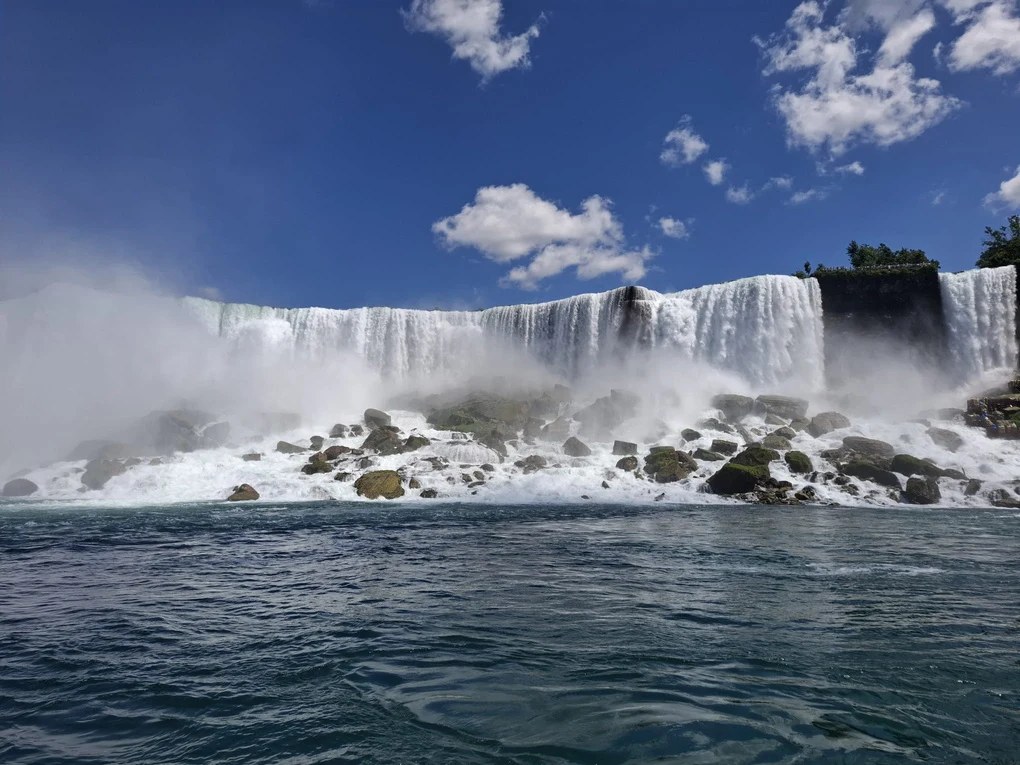 A broad waterfall beneath a blue sky, seen from the water.