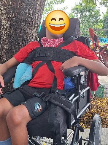 Sam outdoors in his wheelchair, with his face covered in the supplied photograph.